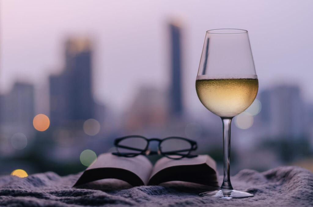Ein Glas Weißwein mit Buch und Brille auf das Bett gelegt