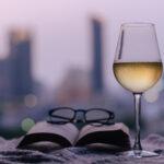 Ein Glas Weißwein mit Buch und Brille auf das Bett gelegt