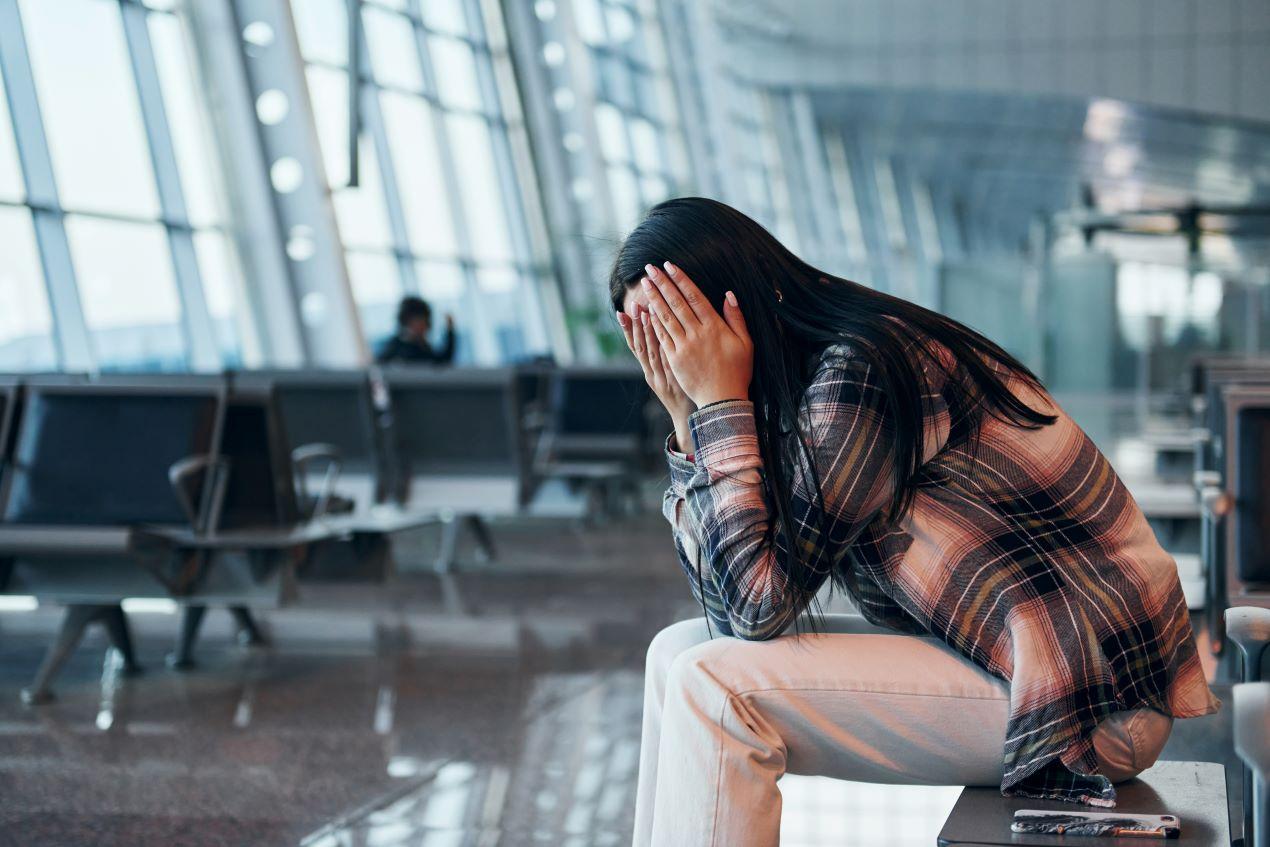 Eine Frau sitzt verzweifelt in einem Flughafen und hält sich den Kopf. Kanzlei Ra-Hartung bietet Unterstützung bei Flugausfällen und Reisemängeln.